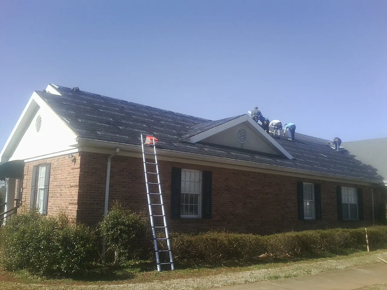 Crew tearing shingles off a brick ranch roof with a ladder set — Emergency Roof Repair work by our crew in Mica