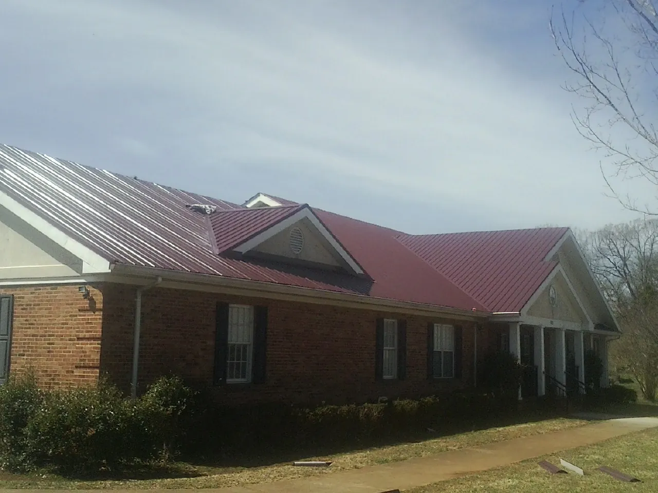 Red metal roof with gabled entries on a long brick building, from a Hail Damage Roof Repair job in Mica