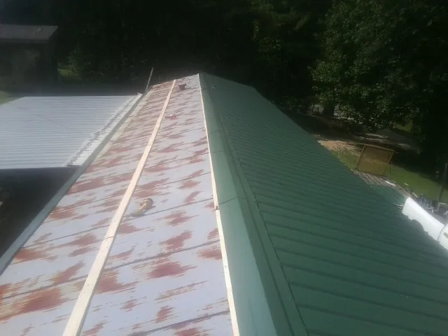 Old rusted panels beside newly installed green metal roofing — Wind Damage Roof Repair by Roofing Brothers in Mica