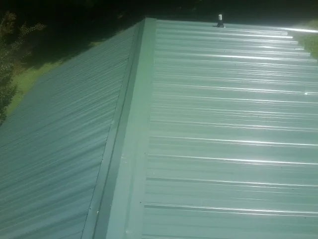 New green metal panels meeting at the ridge of a roof — Flat Roof Repair work by our crew in Mica