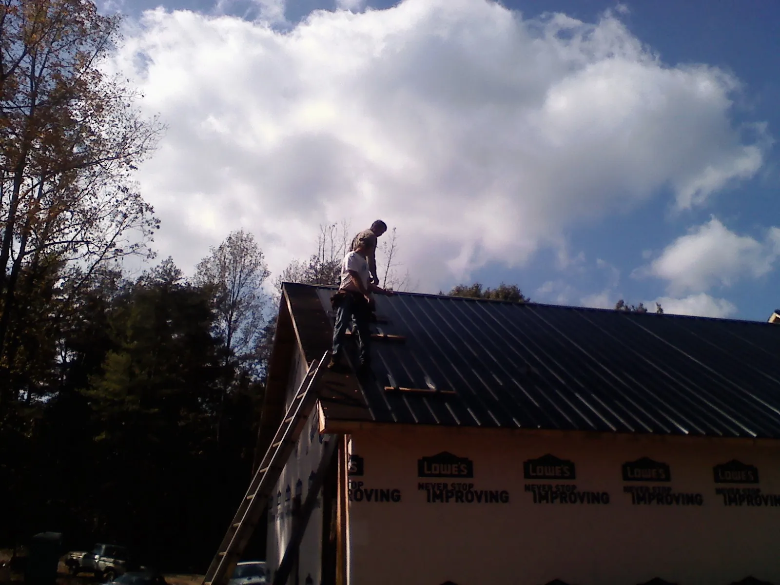 Roofer fastening dark metal panels high against a cloudy sky, from a Roof Inspection job in Mica