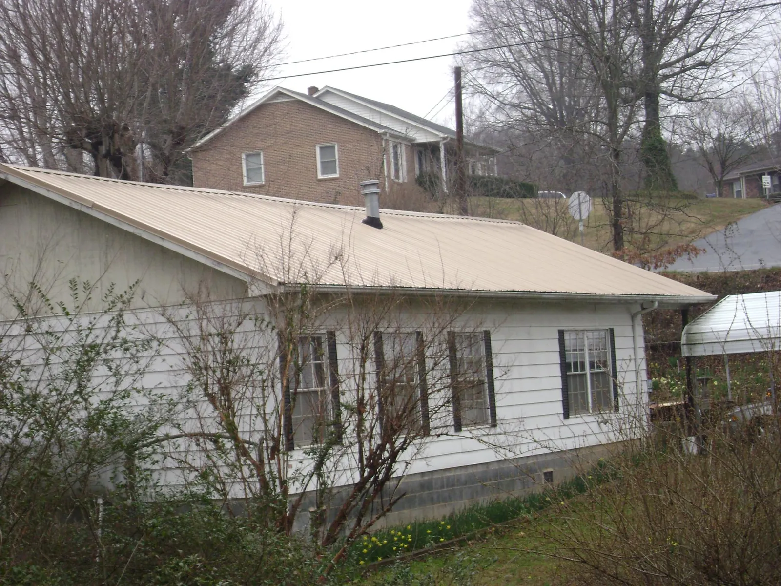 Tan metal roof on a white sided house set into a hillside — Commercial Roofing by Roofing Brothers in Mica